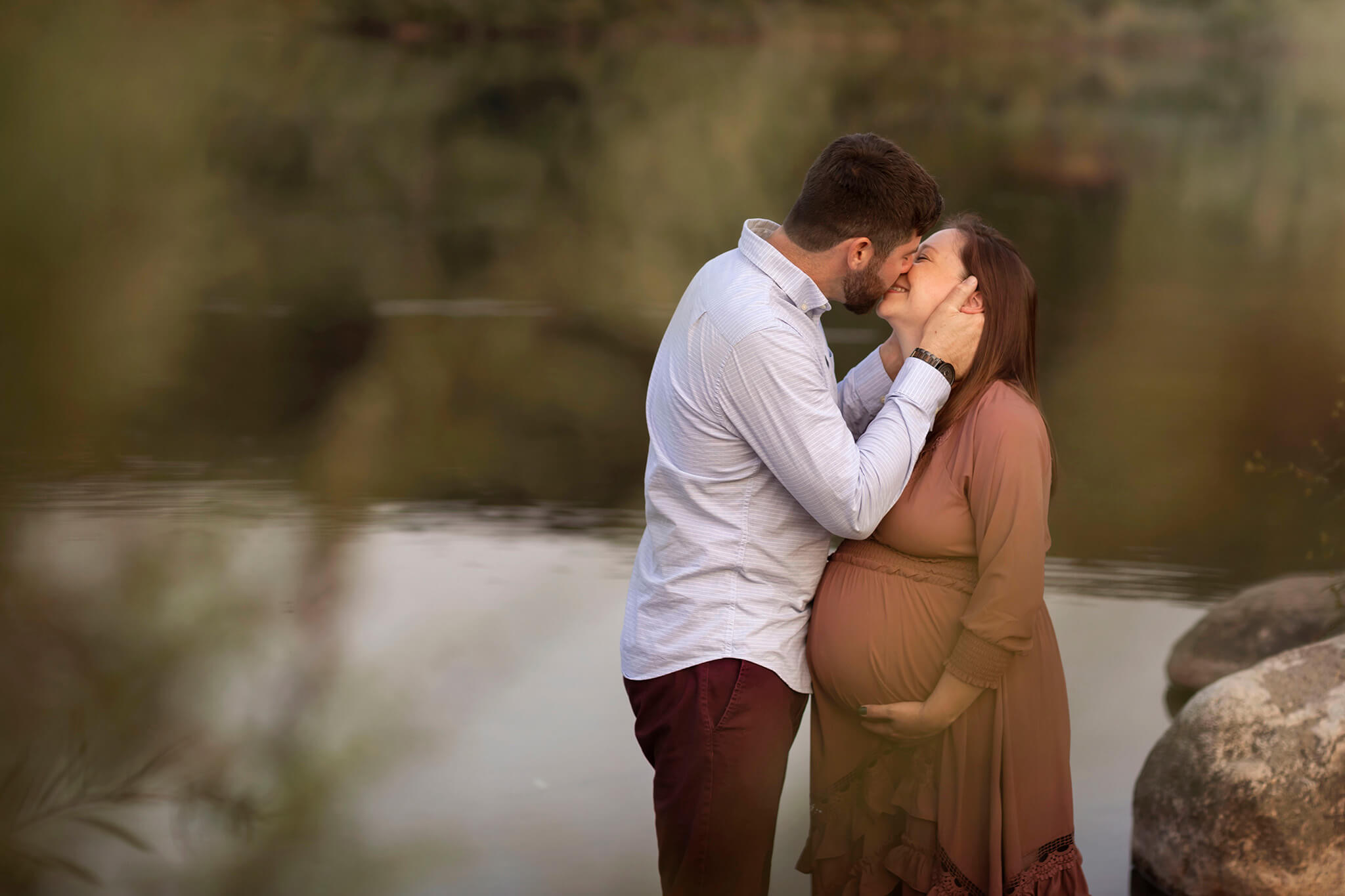 Husband and expecting wife kiss in a lake