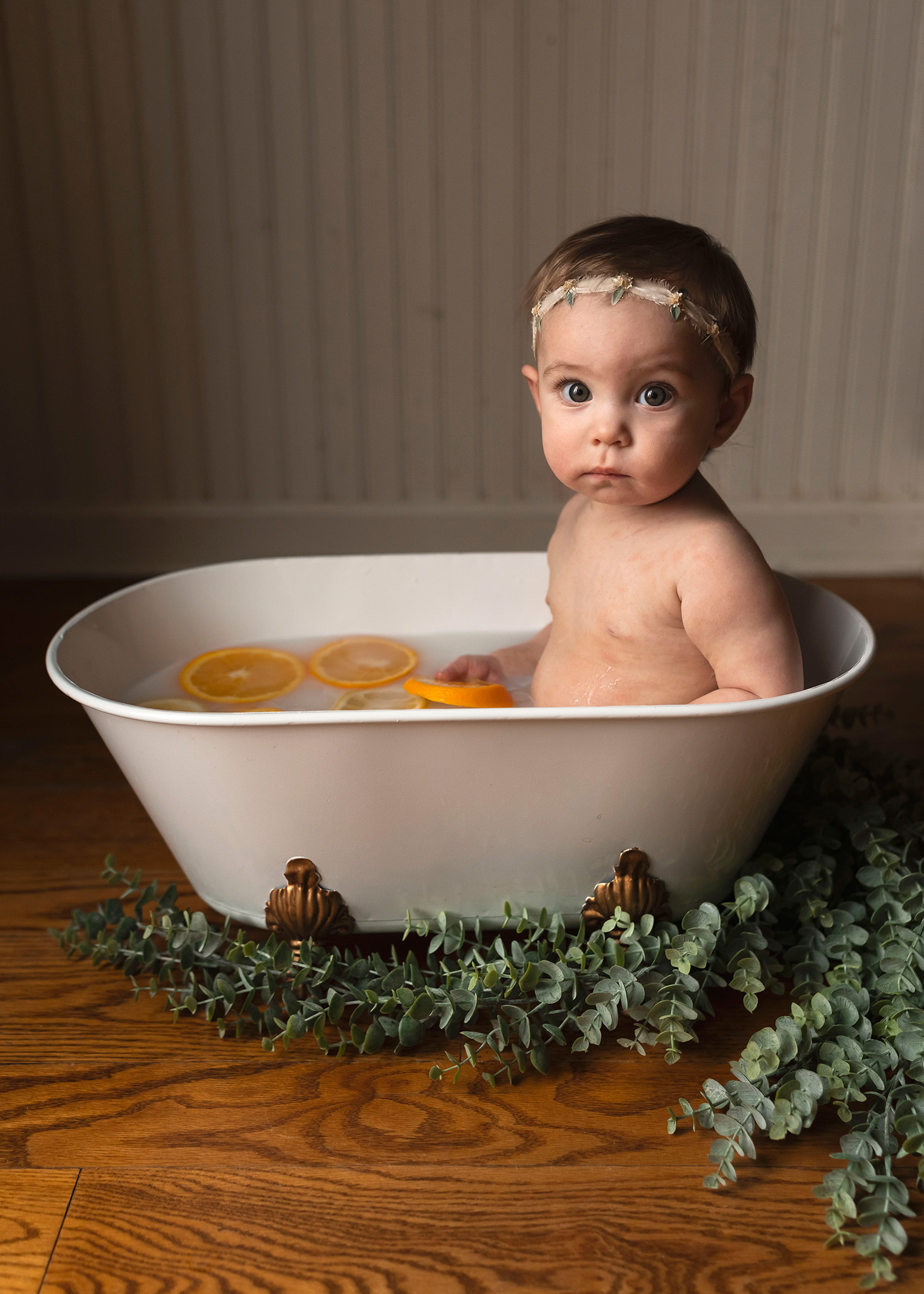 Baby holds orange as she sits in small clawfoot tub