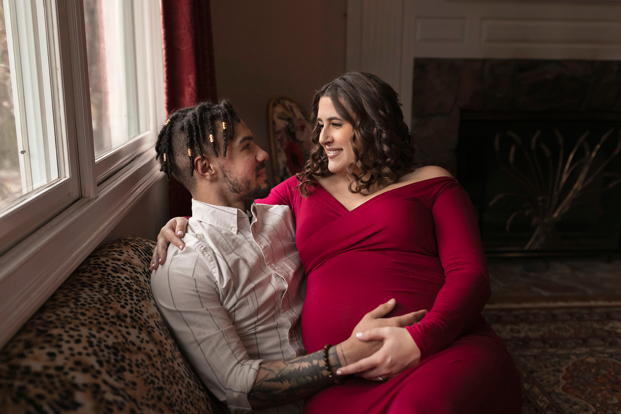 Expecting mom and dad hold onto the belly while sitting on a couch I Maternity Photoshoot NJ