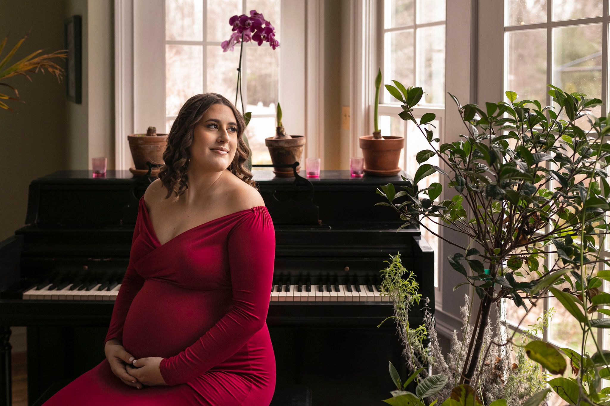Expecting mom sits by piano and is surrounded by plants and flowers I Maternity Photoshoot NJ