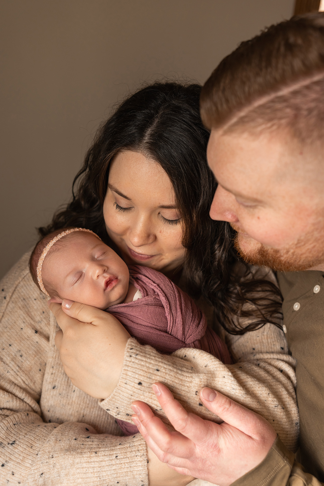 A newborn baby girl sleeps in mom's arms while dad leans in