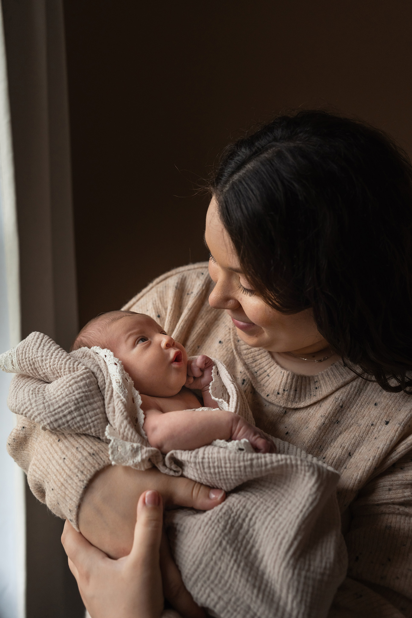 A newborn baby laying in mom's arms looks up to smiling mother after getting 3d ultrasound northern nj