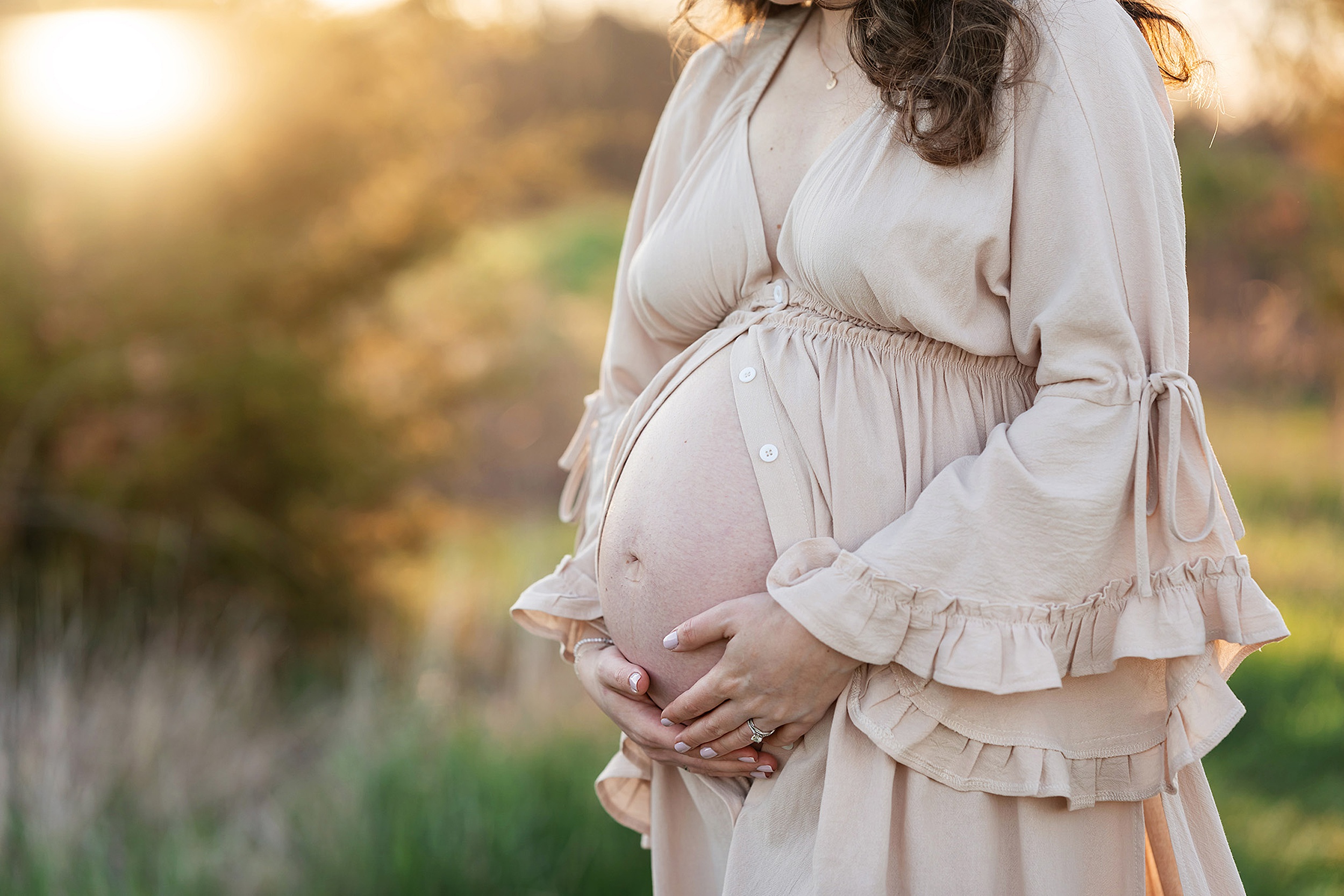 A mom to be opens her dress to hold her bump in a park at sunset after finding midwives in nj