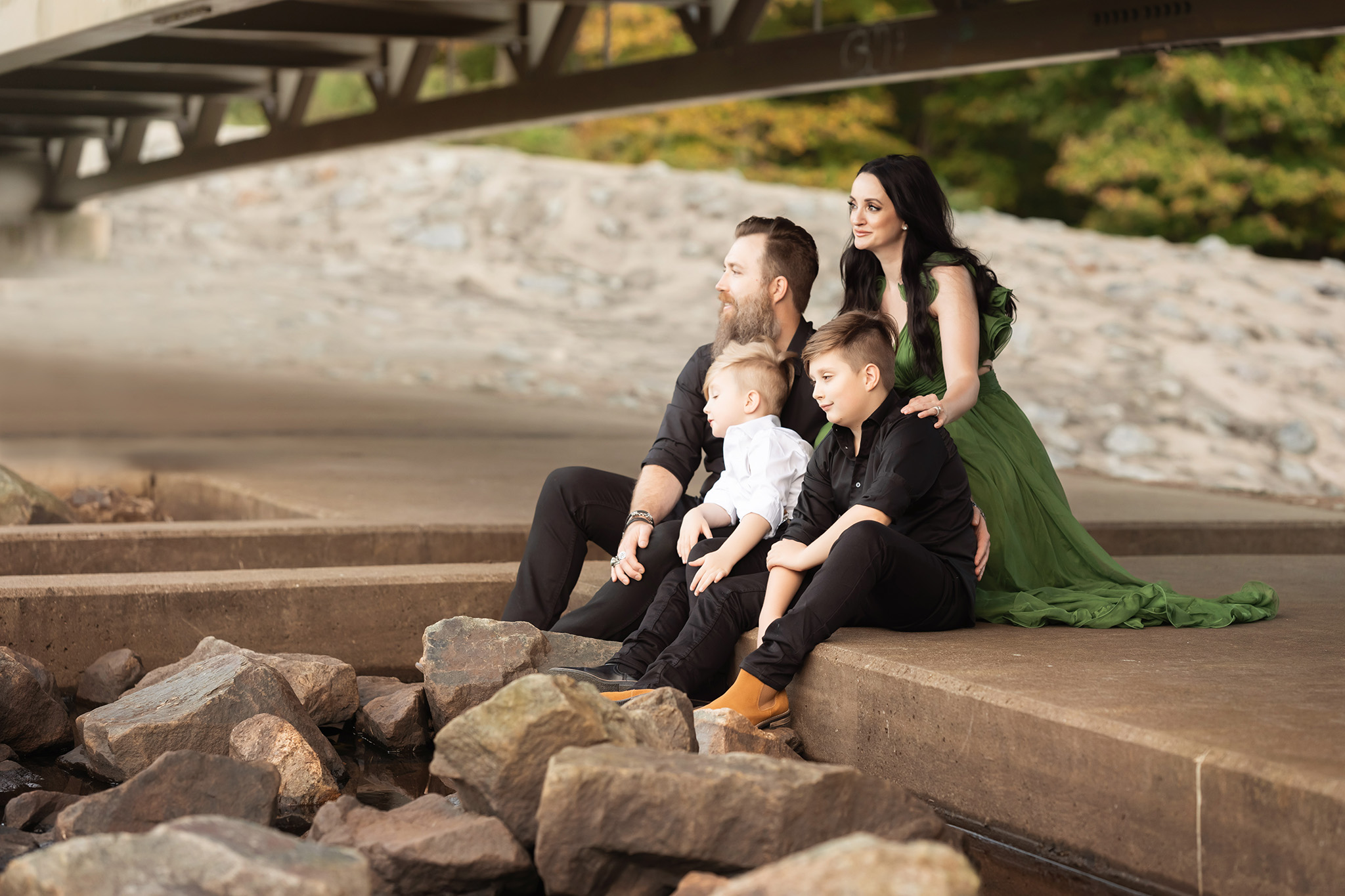 Two toddler boys sit under a park bridge with mom and dad