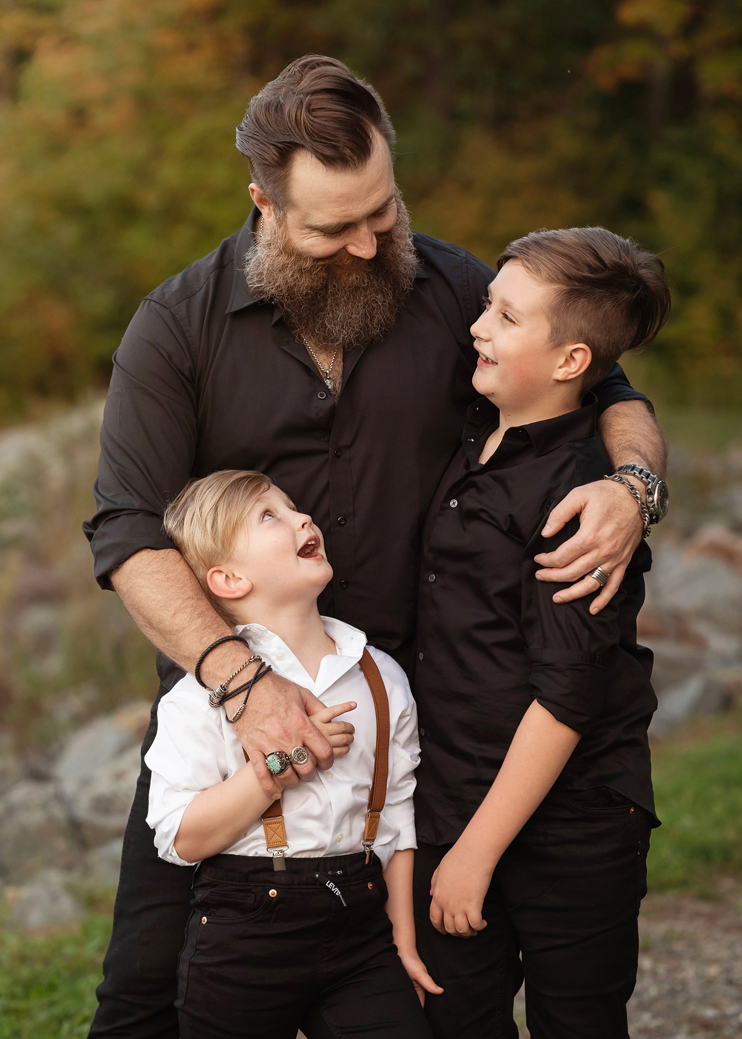 A bearded father hugs his two young sons in black while standing in a park after visiting pediatricians morris county nj