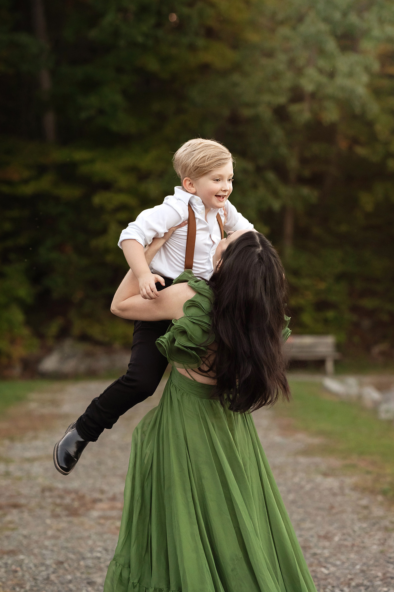 A mother in a long green dress lifts her toddler son while playing in a park path before visiting pediatricians morris county nj