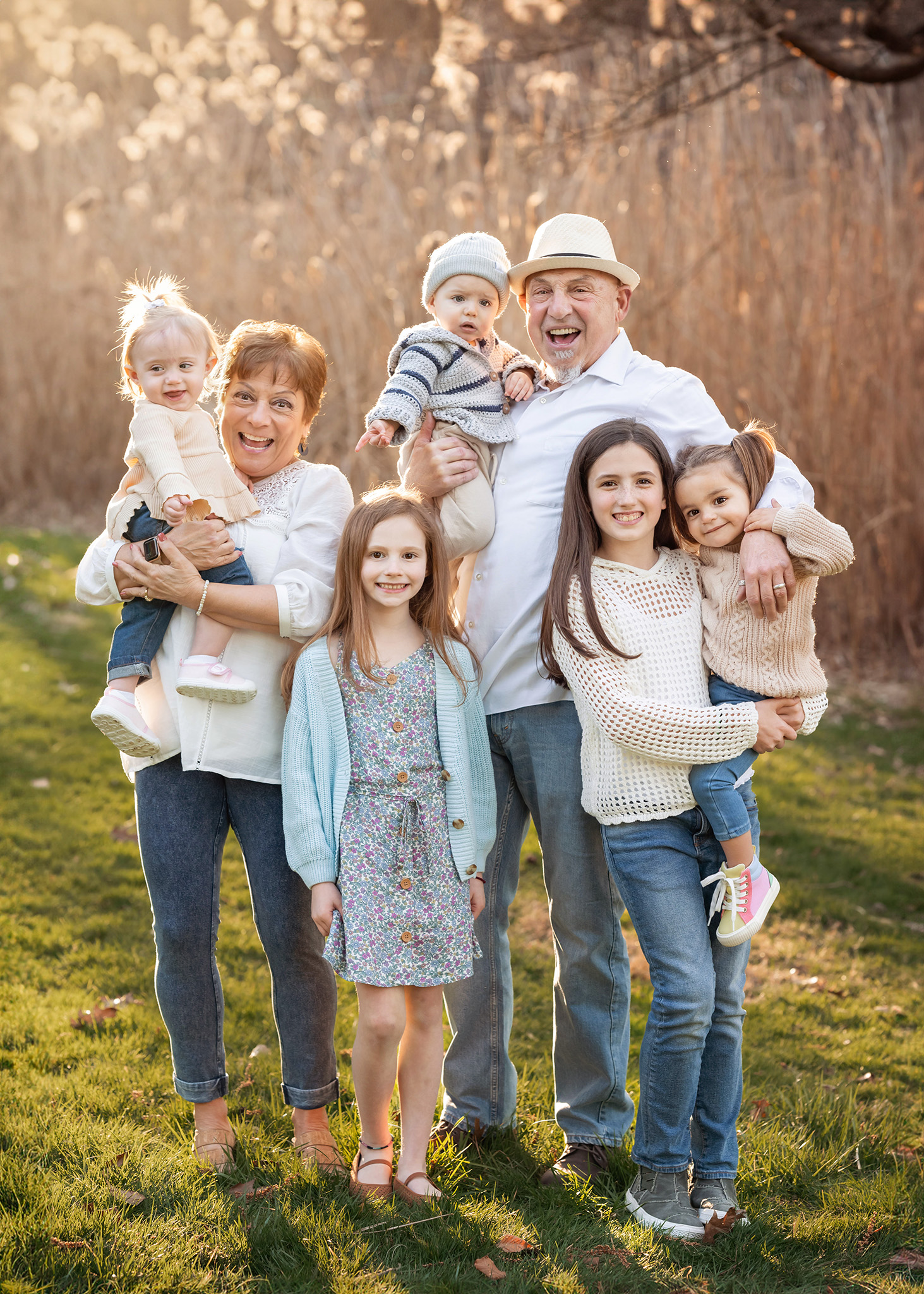 Happy grandparents smile big with their 5 grandchildren hanging all over them in a park at sunset thanks to fertility acupuncture nj