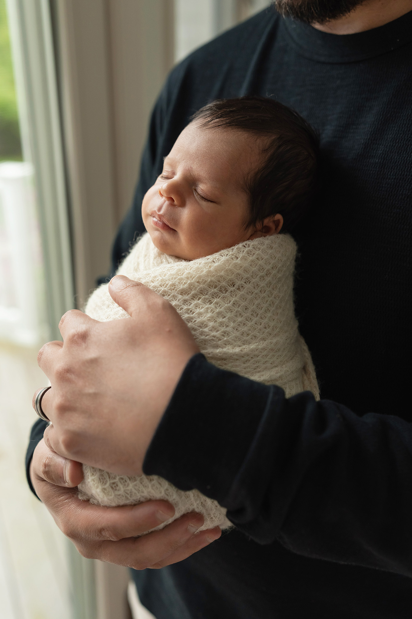 A newborn baby in a white swaddle sleeps while cradled against dad's chest thanks to lactation consultant nj