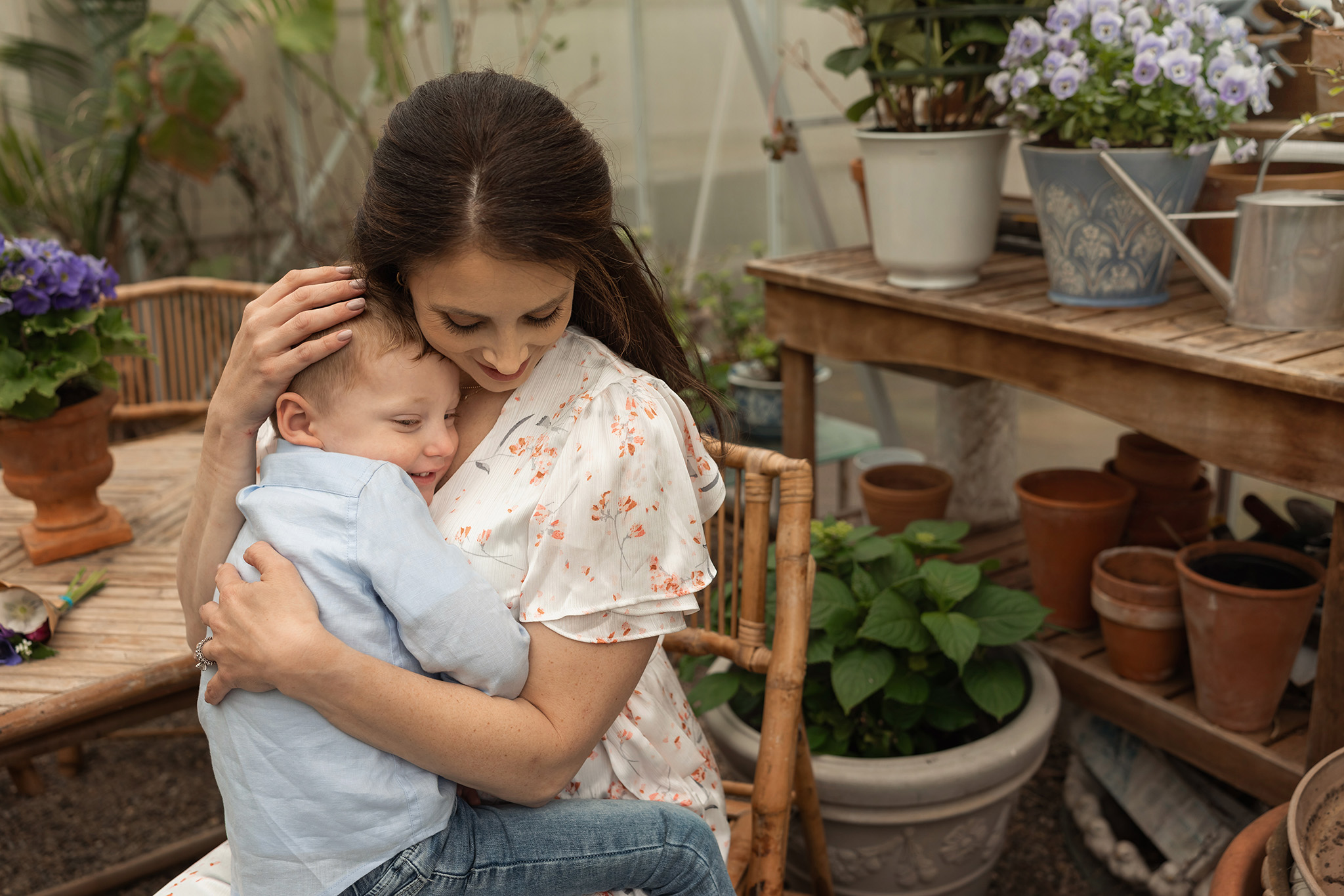 A mother in a white dress sits in a wicker chair in a garden house hugging her toddler son in her lap thanks to obgyn northern nj