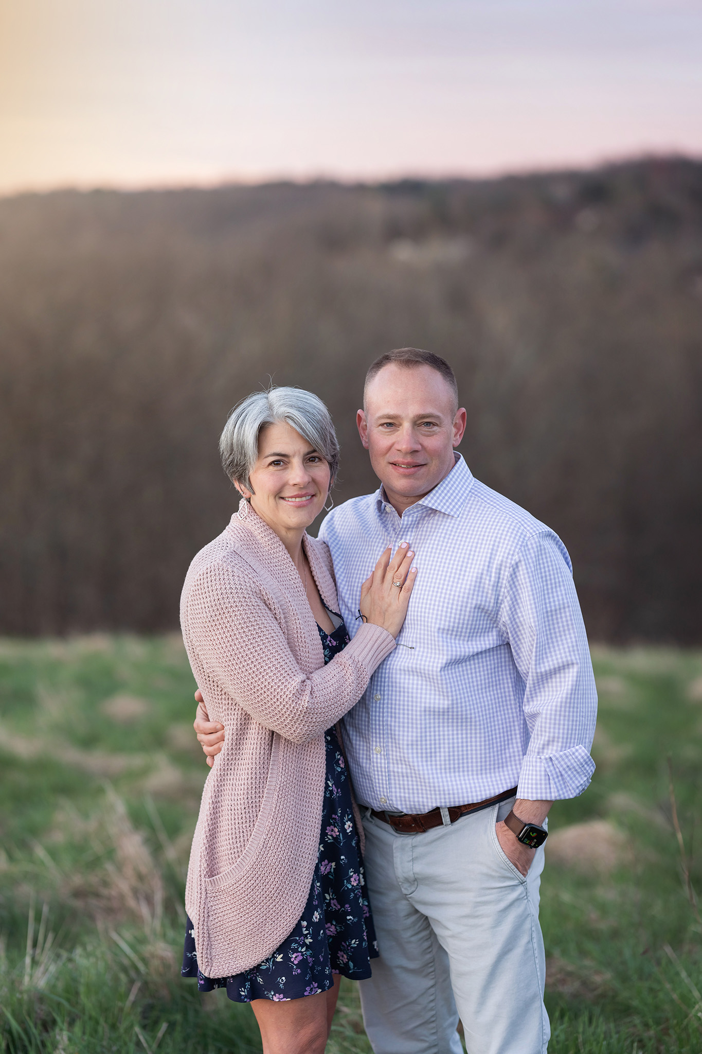 Happy parents stand together smiling on a hill at sunset after taking parenting classes nj