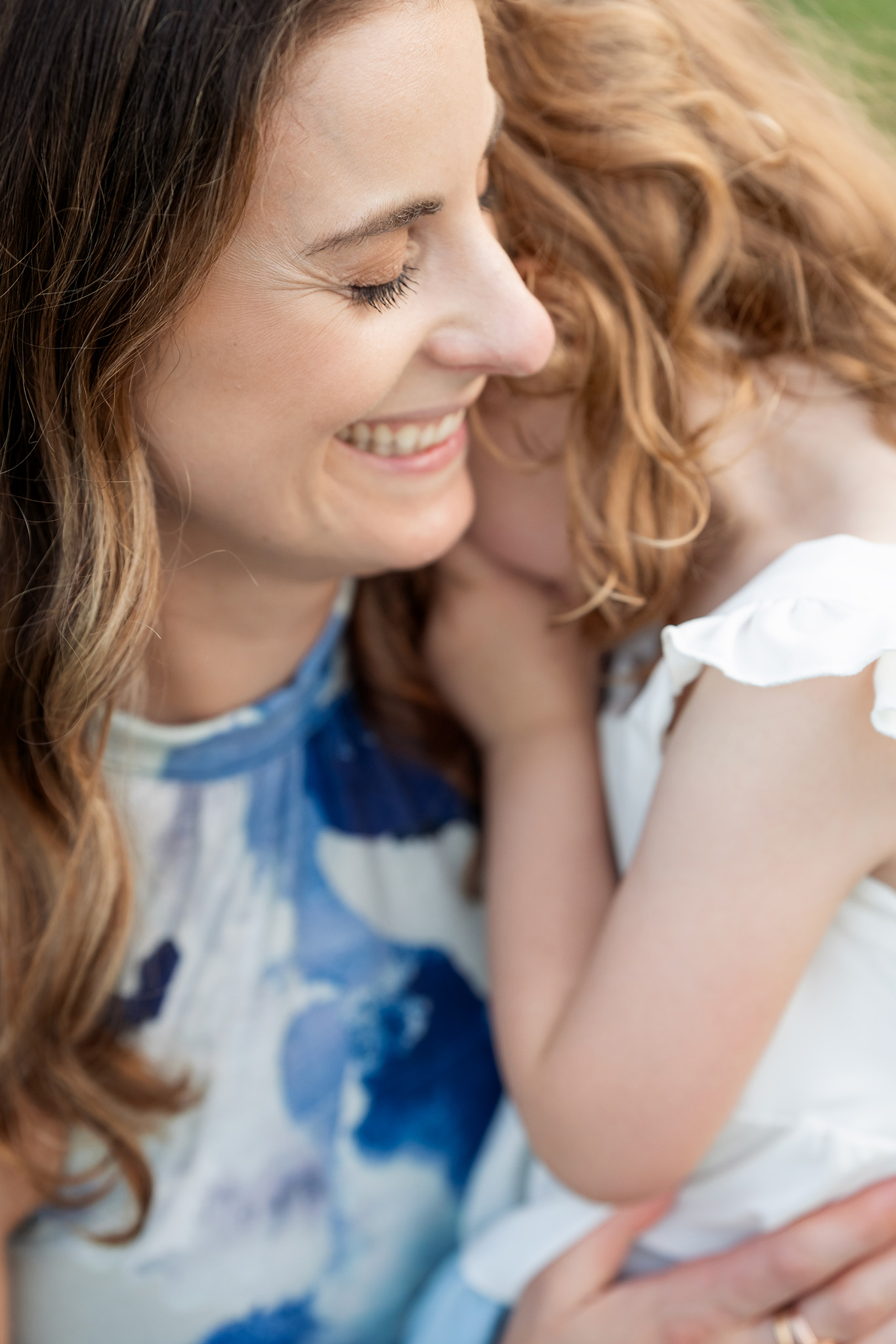 A happy mother smiles while snuggling her shy toddler daughter in her arms