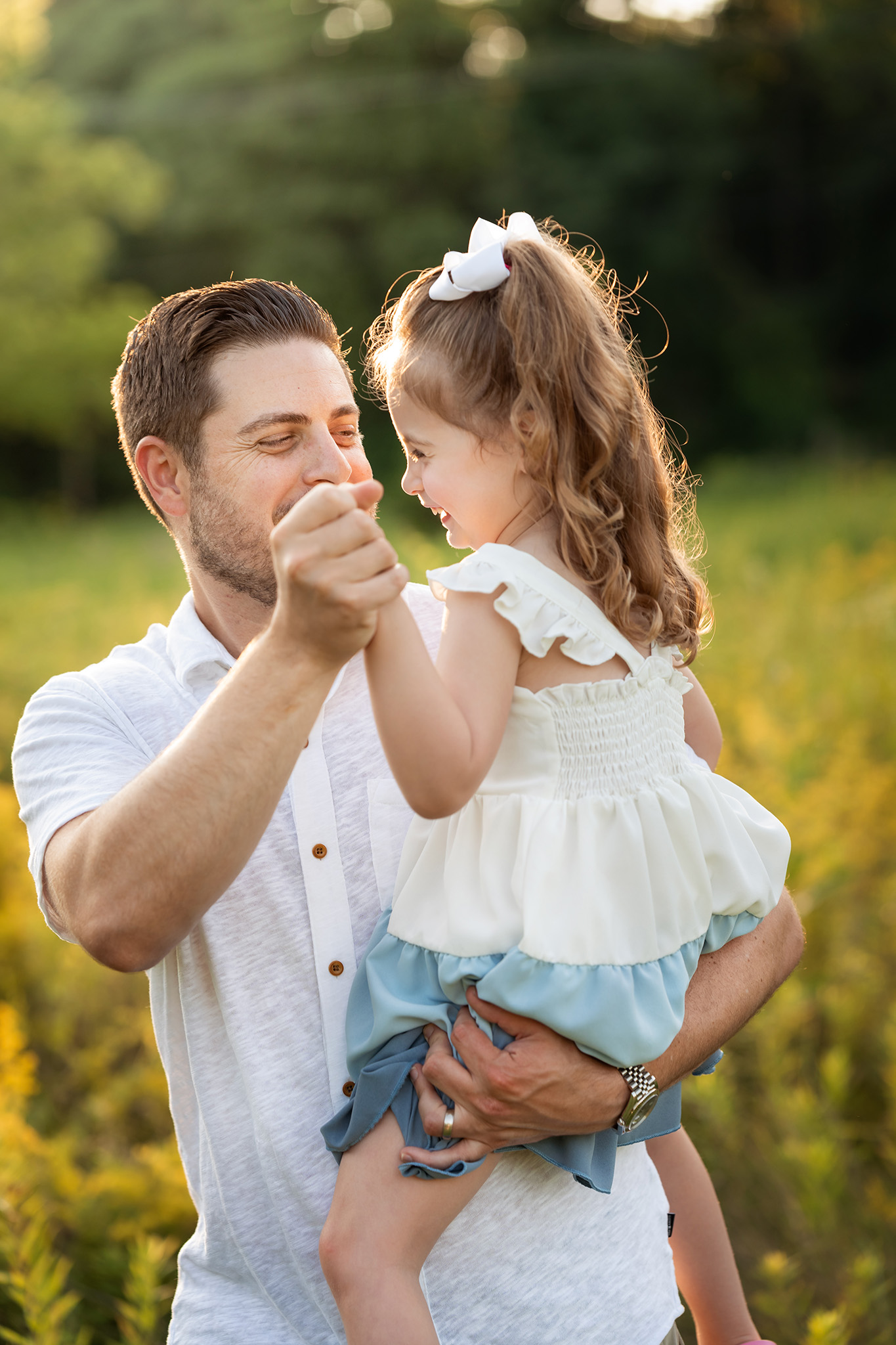 A happy toddler girl dances with dad in a field at sunset while sitting in his arms thanks to a pediatric chiropractor nj