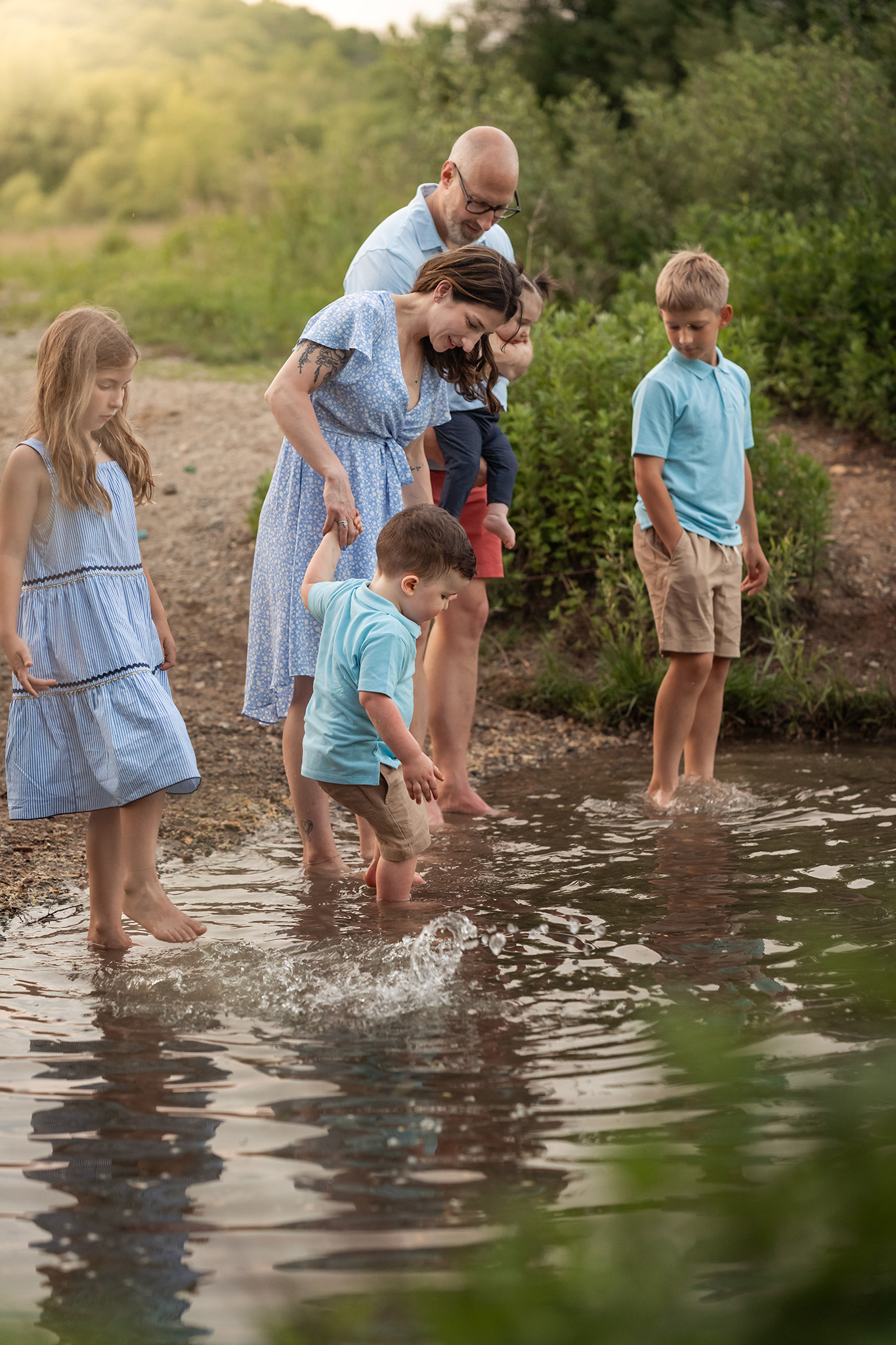 A family of 6 explore the water in a park at sunset in blue shirts after visiting a pediatric dentist northern nj