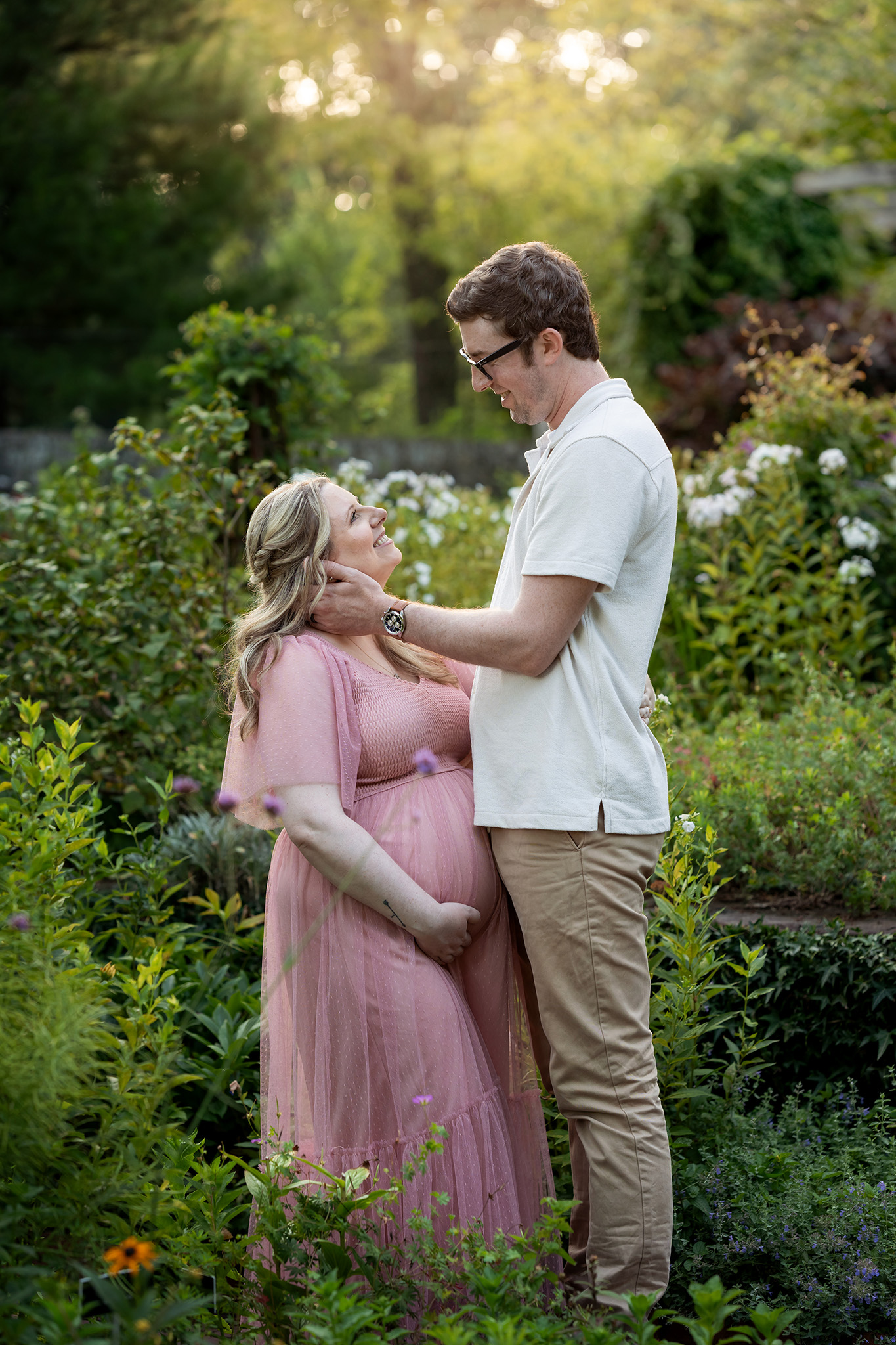 Happy expecting parents smile at each other while standing in a flower garden