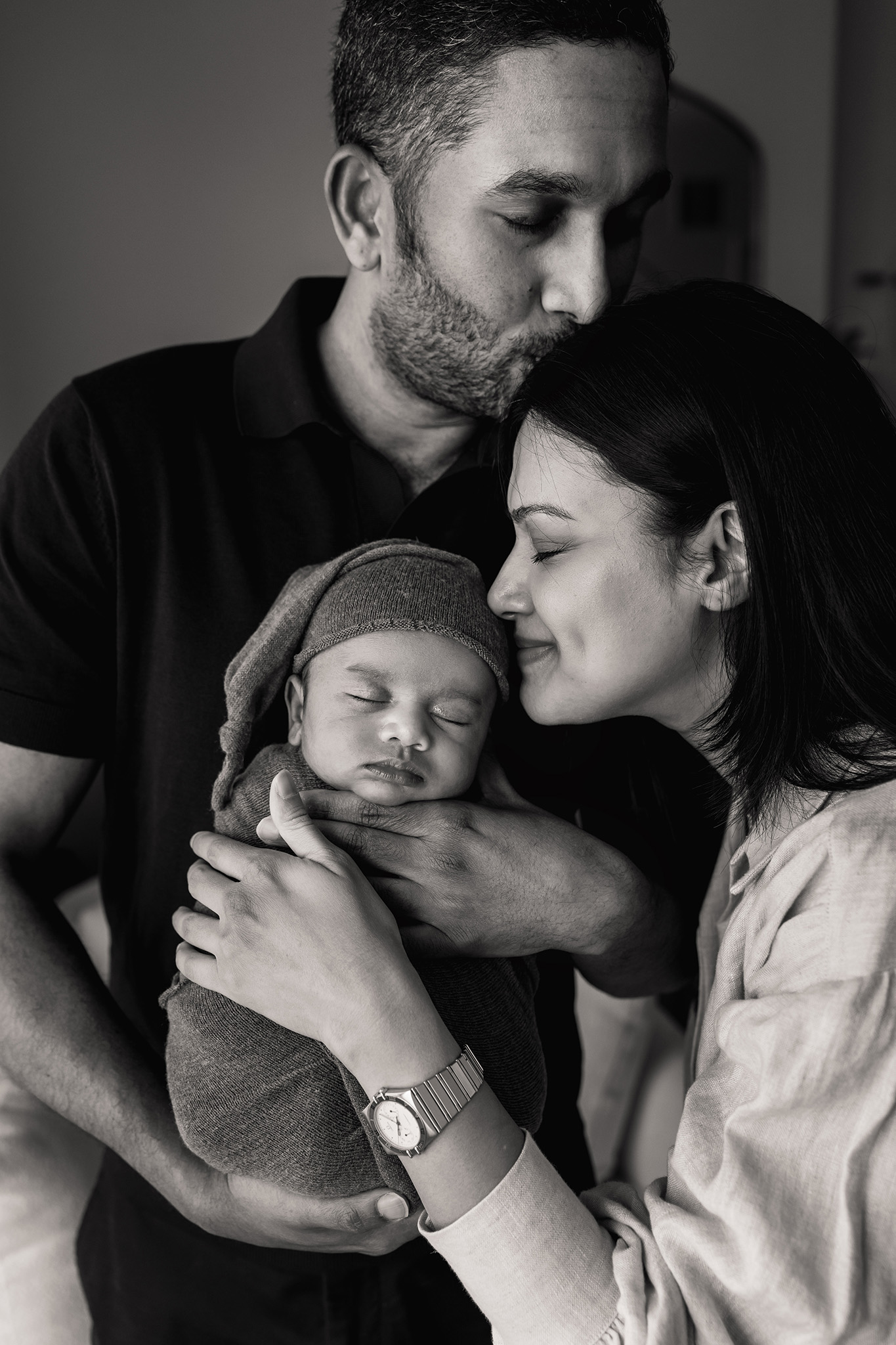 Happy new parents snuggle their sleeping newborn baby against dad's chest