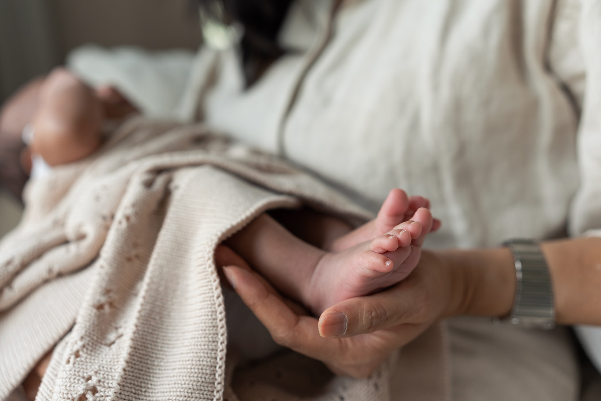 Details of a mother holding the feet of her newborn baby in her lap thanks to a prenatal chiropractor nj