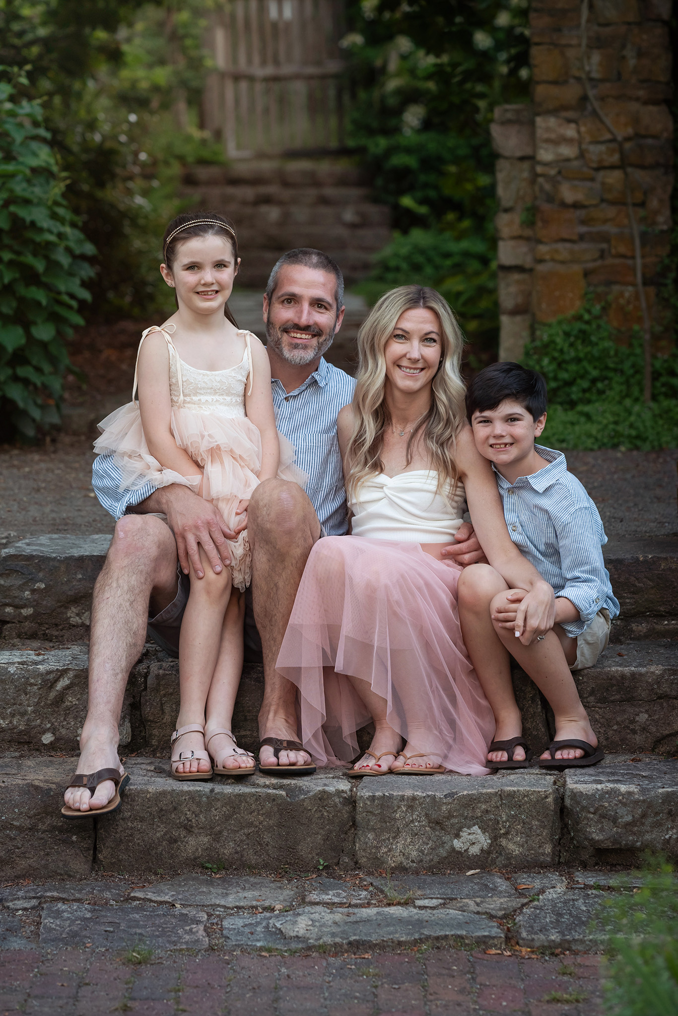 A happy family of four sit on stone garden steps smiling