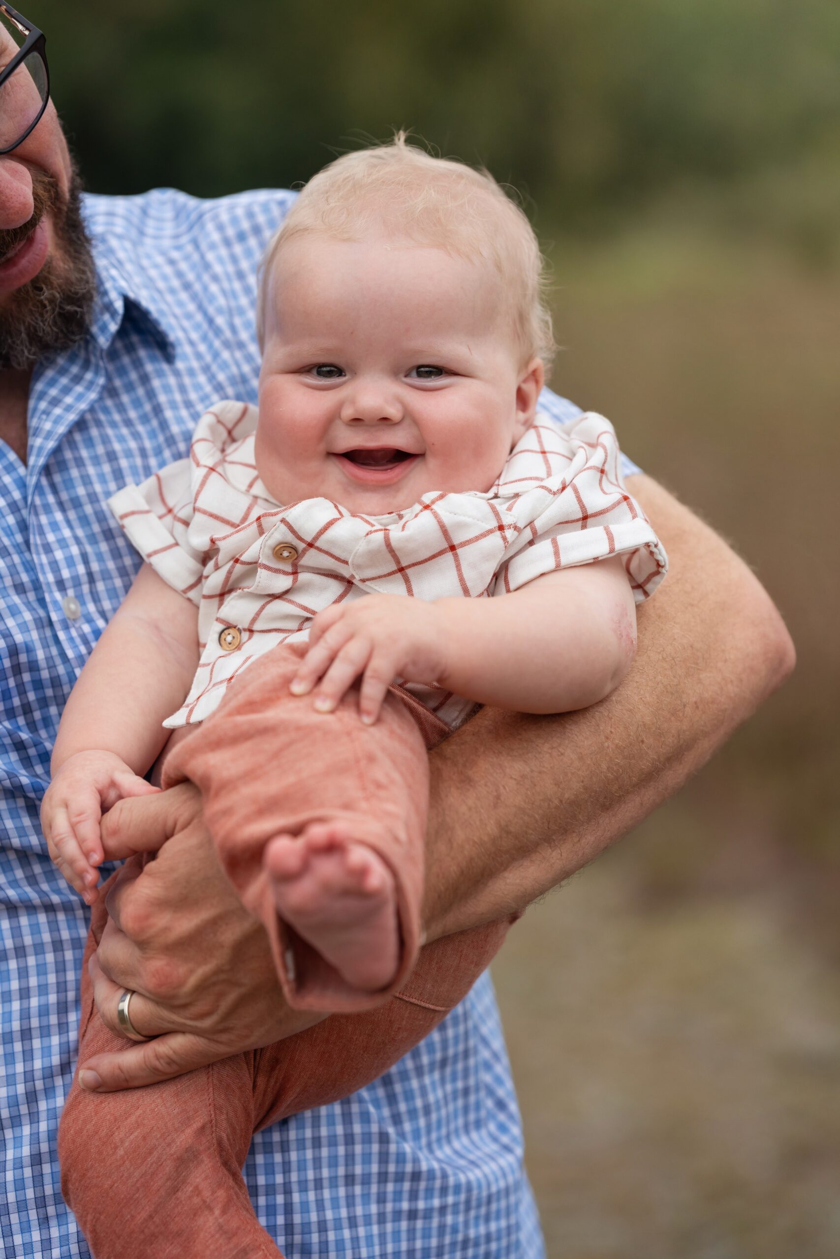 A happy baby sits in dad's arms in a striped shirt during fun things to do in nj with toddlers