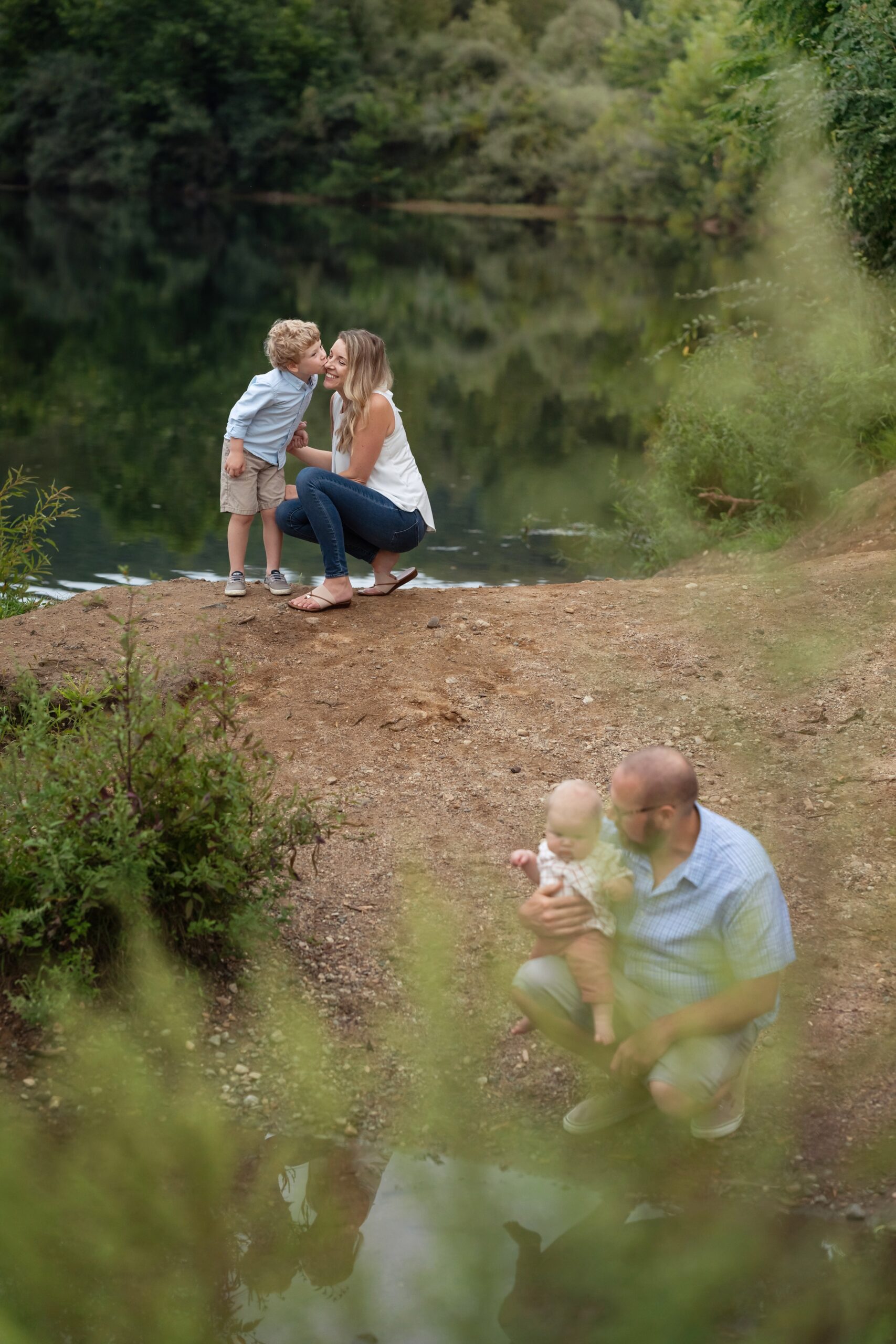 A young boy kisses mom by a pond edge while dad explores the another with baby during fun things to do in nj with toddlers