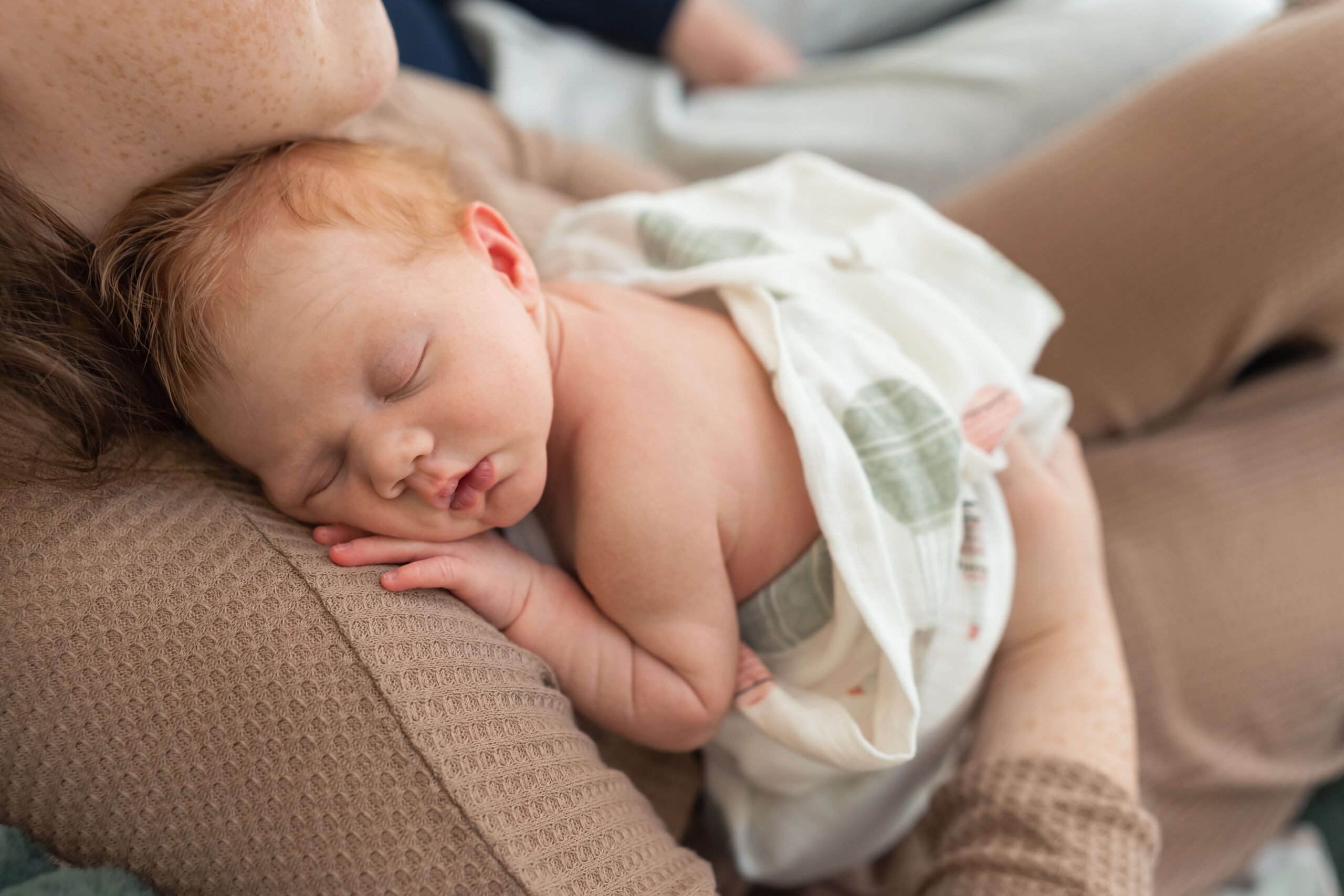 A sleeping newborn rests his head on mom's shoulder while sleeping