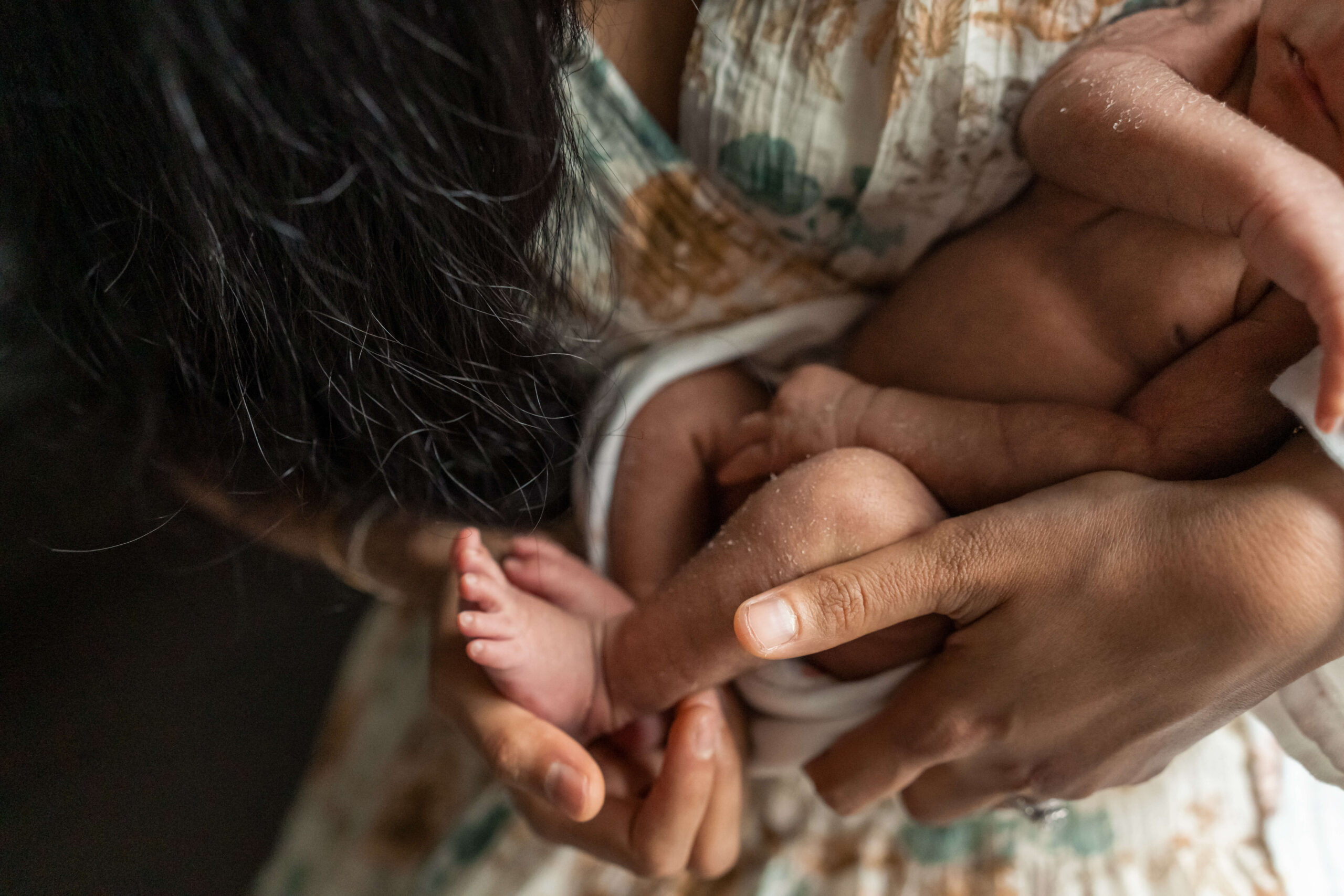 Details of a newborn baby's legs in mom's hands against her chest