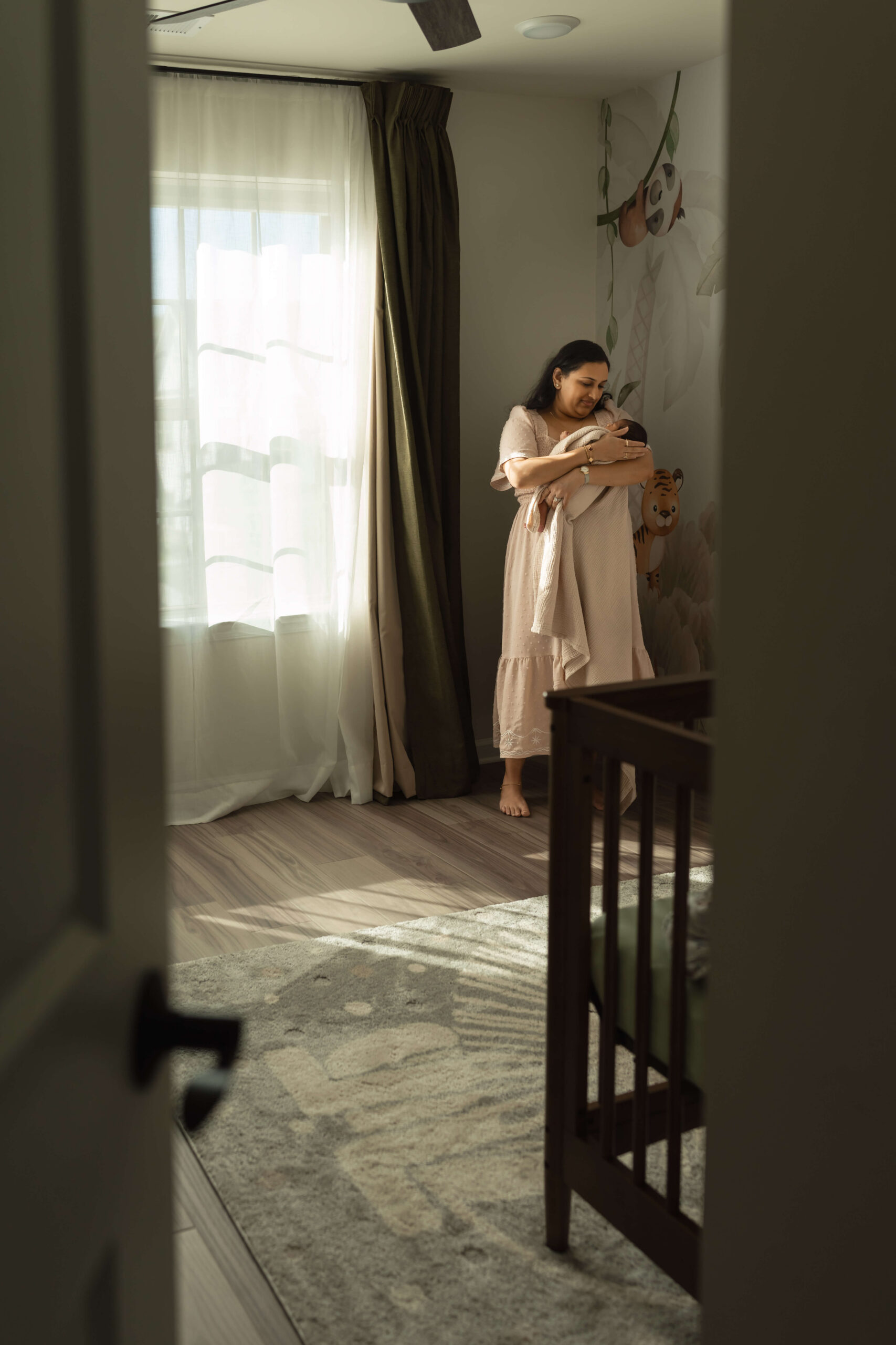 A happy new mom stands in a nursery corner holding her sleeping newborn in her arms