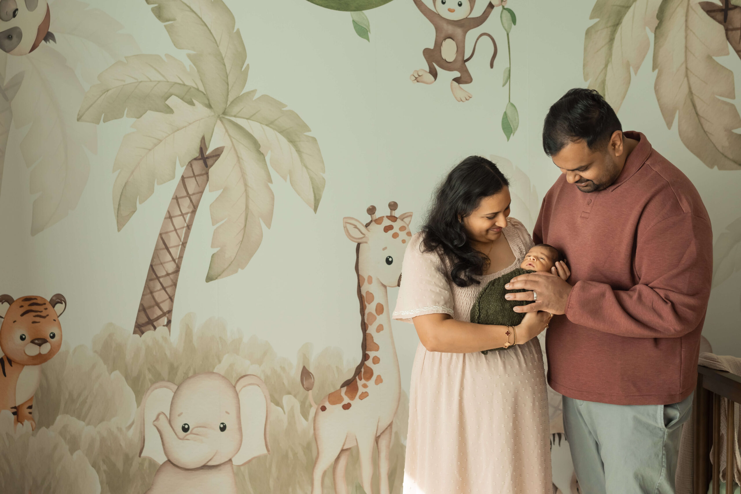 A mom and dad cradle their sleeping newborn while standing in their jungle themed nursery after finding mom groups in morris county nj