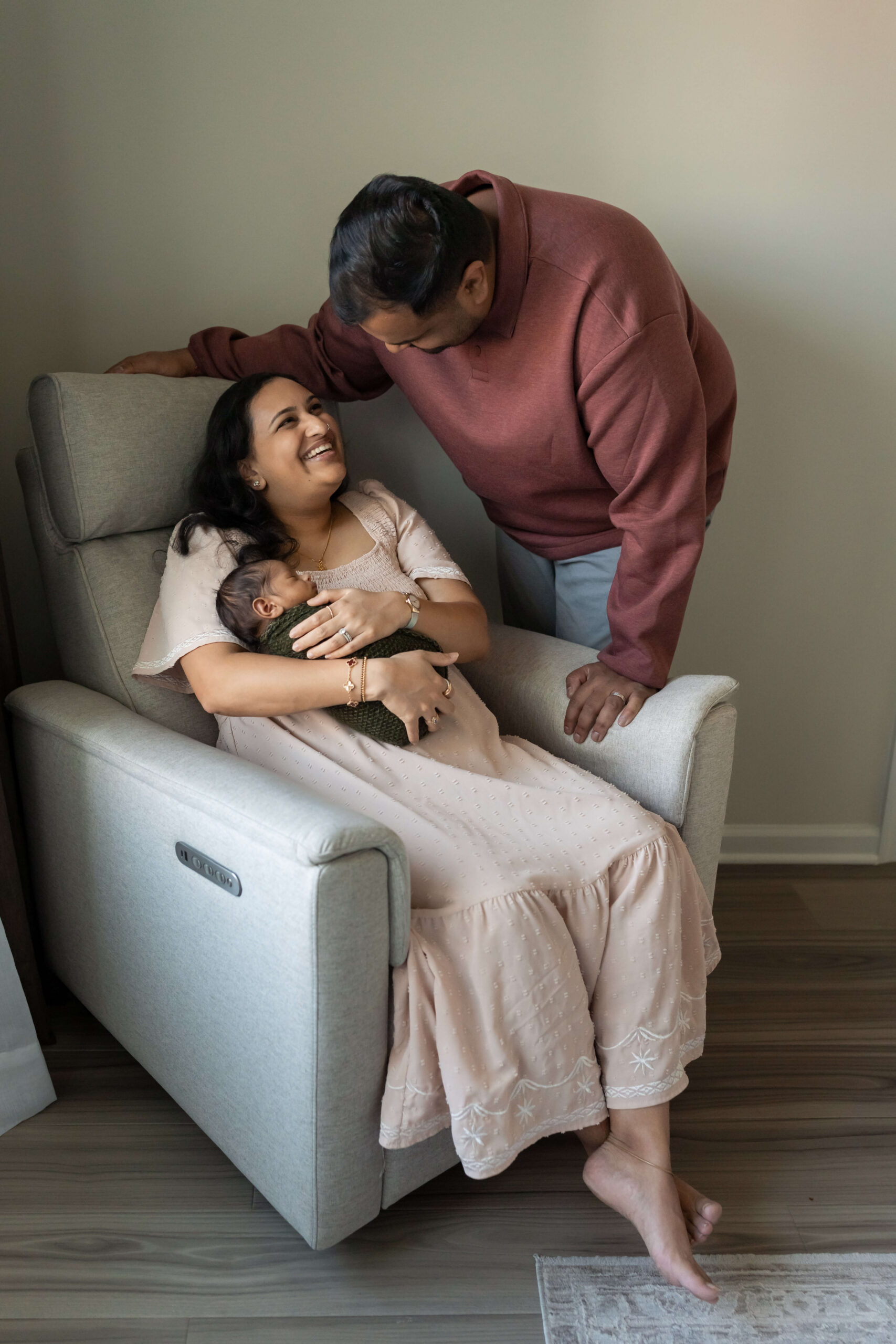 A happy new mom looks up to dad leaning over her while cradling their sleeping newborn in her arms after finding mom groups in morris county nj