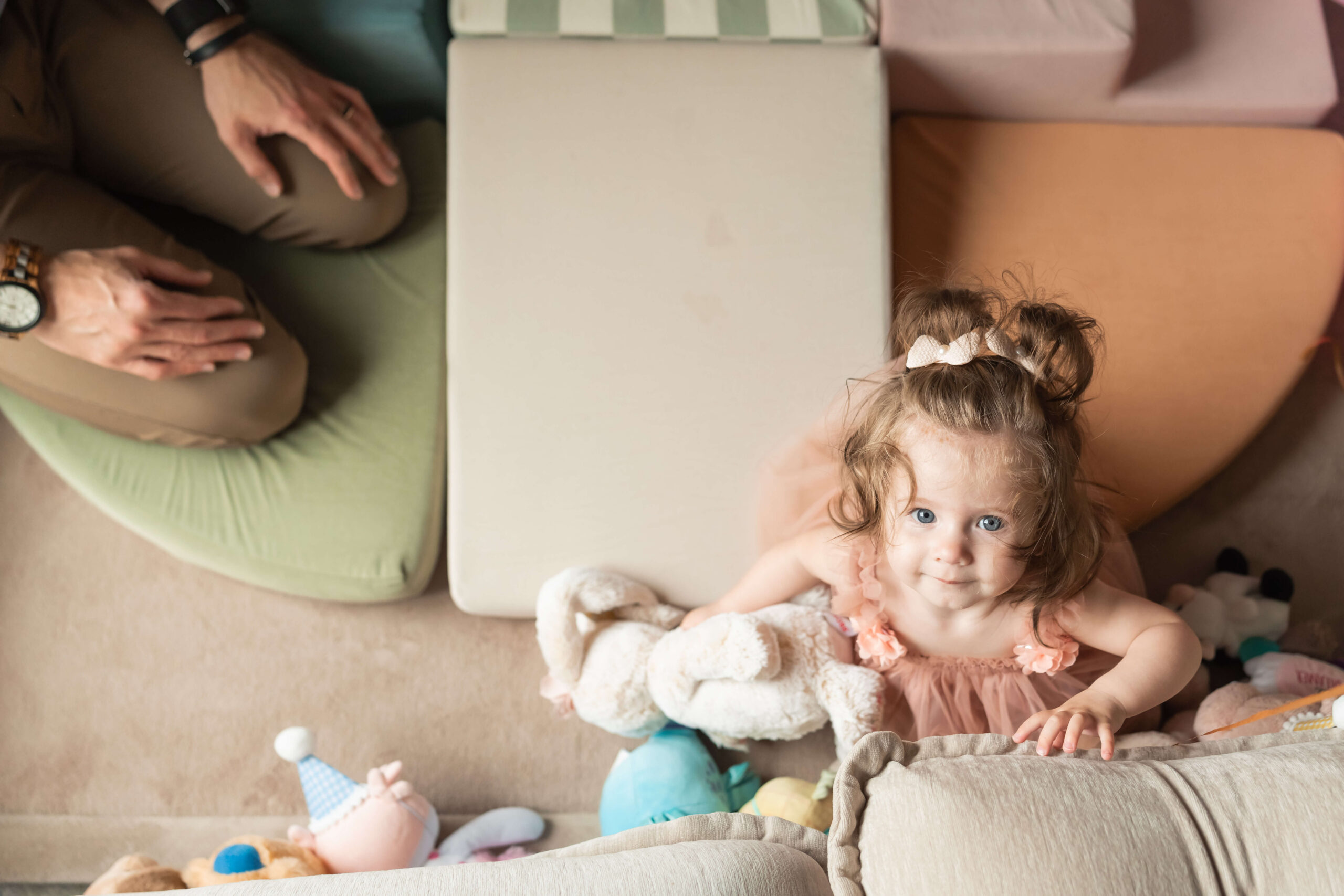 A look down at a happy toddler girl in a pink tulle dress playing with stuffed animals on the floor